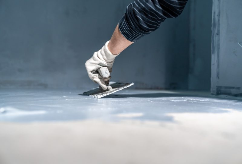 Installer pouring amber epoxy resin from a bucket onto prepared concrete